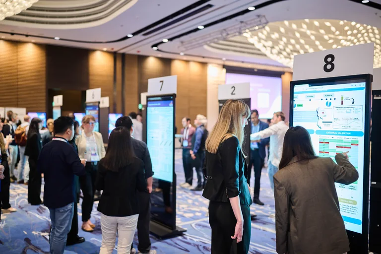 Delegates discussing research at digital poster displays during CNAPS 2025